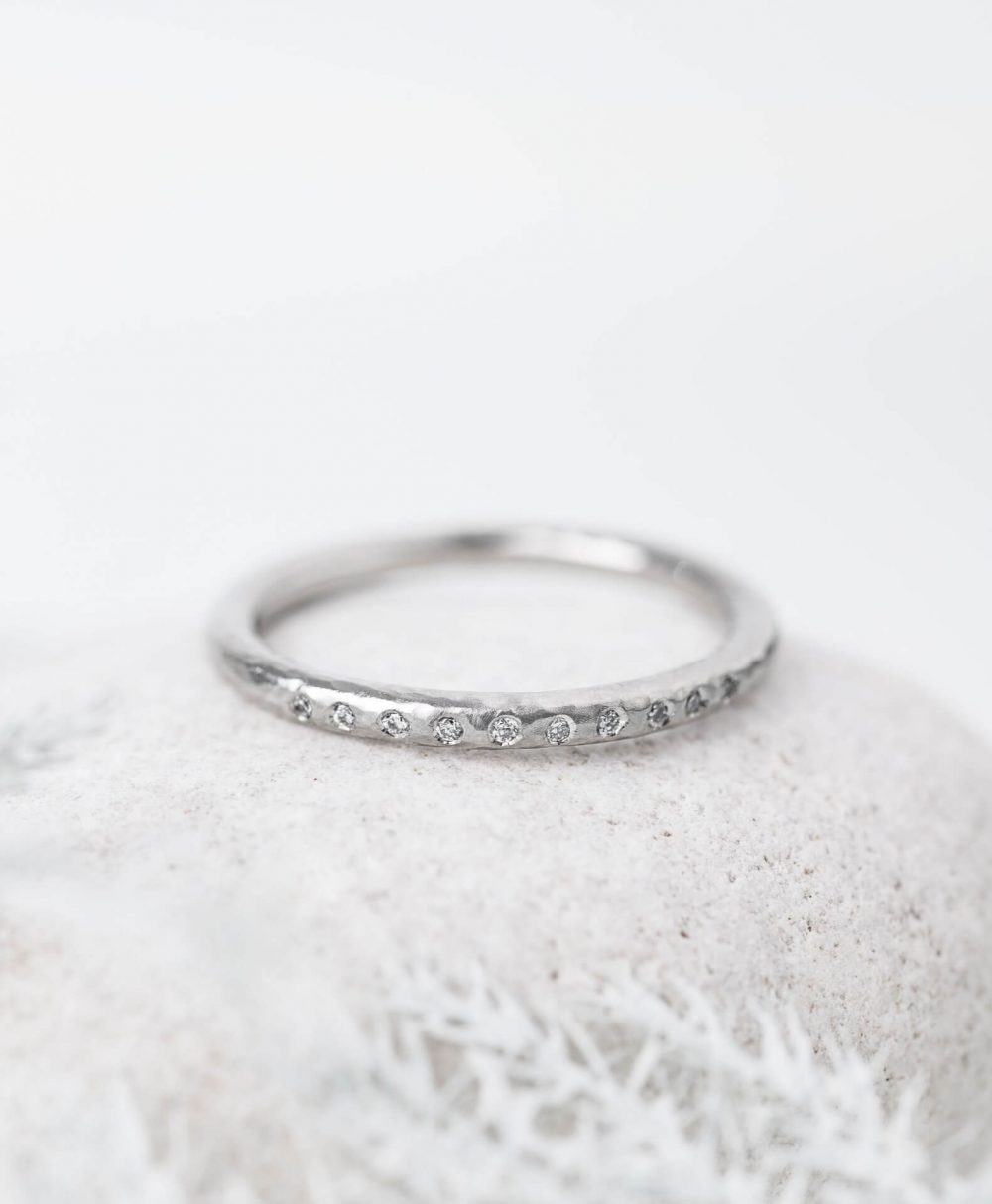 Hammered Diamond Wedding Ring Handmade In Platinum And Set With Ten Sparkle Diamonds, Pictured On Pebble. Designed By Bristol Jeweller Jacks Turner.