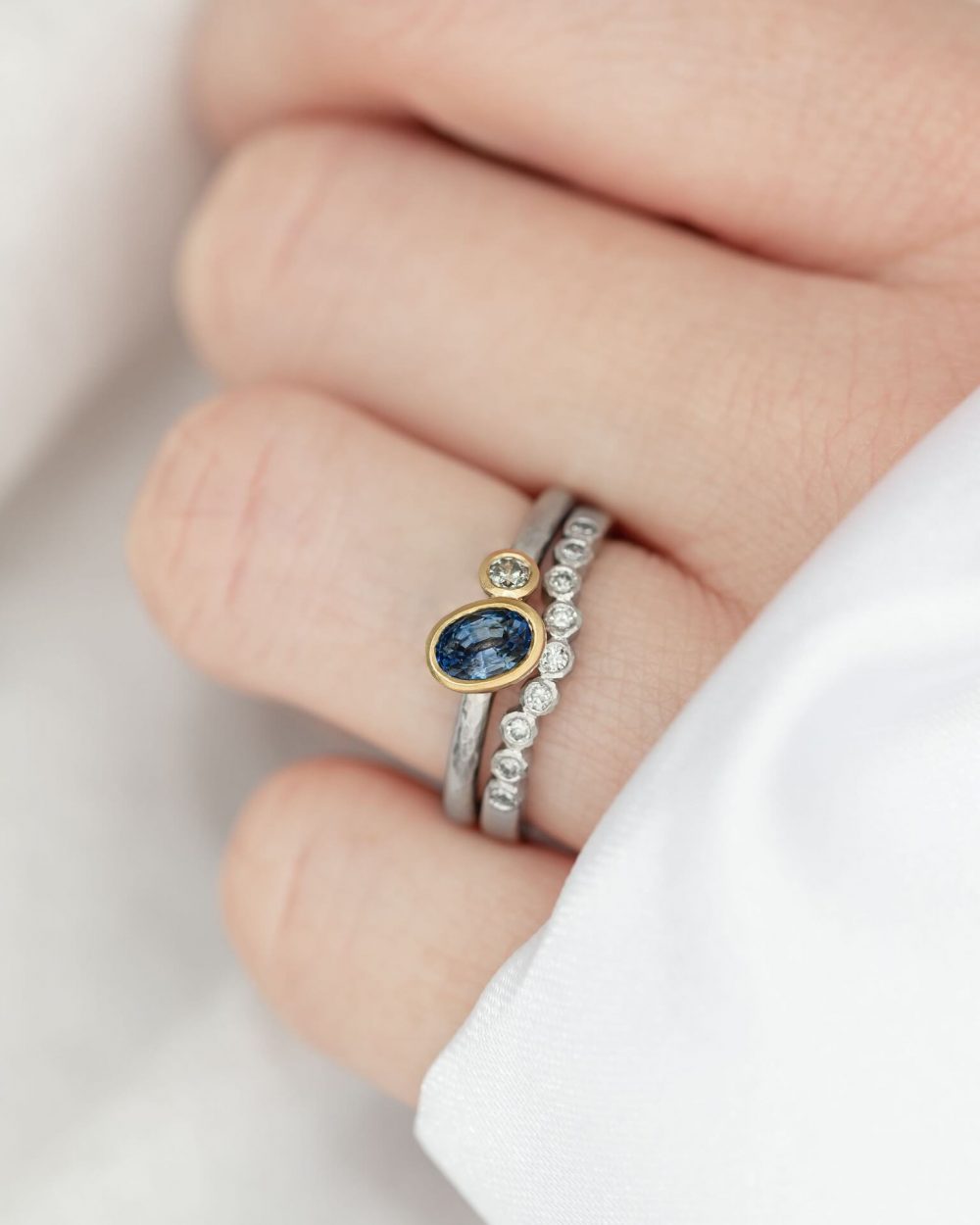 Oval Sapphire Diamond Alternative Engagement Ring Worn With A Curved Salt And Pepper Diamond Ring. Pictured On Model By Bristol Jeweller Jacks Turner.